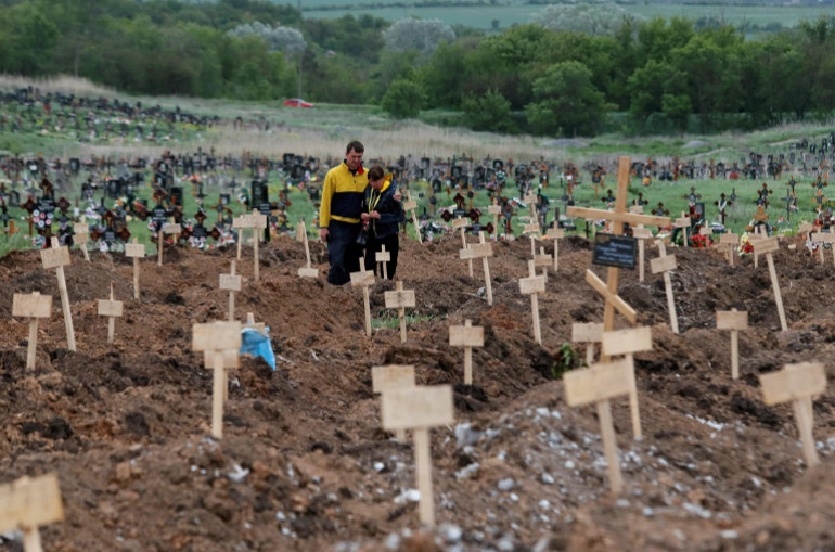 People stand amid newly-made graves in the course of the Russia-Ukraine conflict in Staryi Krym outside Mariupol [File: Alexander Ermochenko/Reuters]